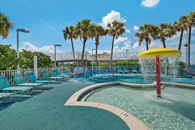 a swimming pool with a fountain and chairs and palm trees at Boardwalk 209 in Panama City Beach