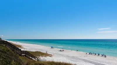 a beach with people sitting on the sand and the ocean at Turtle Beach - 55 Nature Way #100 in Santa Rosa Beach