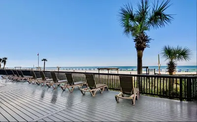 a row of chairs on a boardwalk next to the beach at Sunbird Resort! Incredible Beachfront Corner Unit! Free Beach Chairs! by Dolce Vita Getaways PCB in Panama City Beach