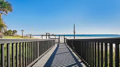 a boardwalk to the beach with a fence and palm trees at Fun N The Sun at Sunbird #1102W by InJoy Vacations in Panama City Beach