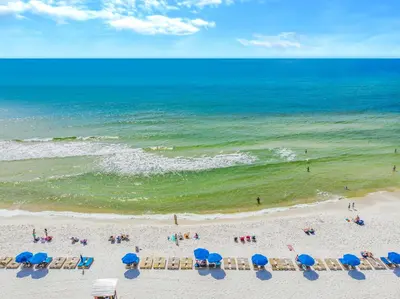 a beach with blue umbrellas and people on the beach at Grand Panama #2-0505 in Panama City Beach