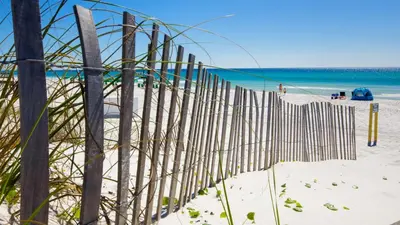 a fence on the beach with the ocean in the background at Beach Haven! 2BR 2BA Sleeps 6! Coastal paradise awaits! in Panama City Beach