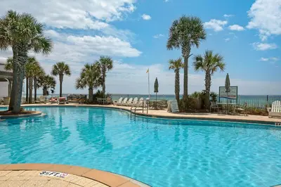 a large swimming pool with palm trees and the ocean at Aqua Resort 906 by Emerald Coast Retreats in Panama City Beach
