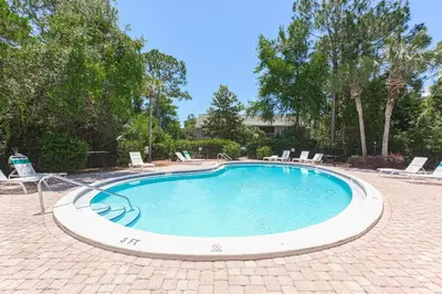 a large swimming pool with chairs and trees at Pelicans Nest II - Easy walk to the beach & Pool in Santa Rosa Beach