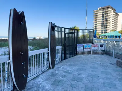 a black gate with a surfboard next to a beach at Edgewater 3-0613 'Solace' in Panama City Beach