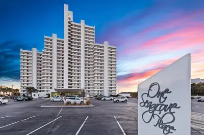 a large white building with a parking lot with cars at One Seagrove Place 1407 in Santa Rosa Beach