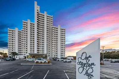 a large white building with a parking lot with cars at One Seagrove Place 1503 in Santa Rosa Beach