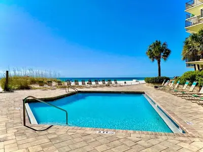 a swimming pool with chairs and the ocean in the background at Pelican Walk 1012 in Panama City Beach