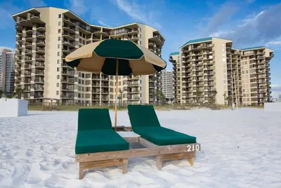 two chairs and an umbrella on the beach with buildings at Sunbird Beach Resort #712 East in Panama City Beach