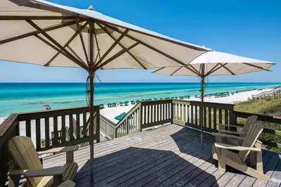 a deck with chairs and umbrellas and the beach at Uncorked Carriage House in Rosemary Beach