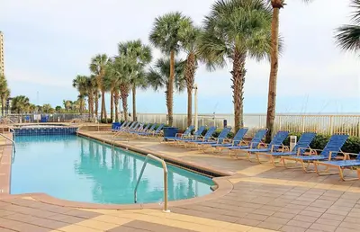 a swimming pool with blue chairs and palm trees at Beachfront Bliss Awaits: 2-Bed, 2-Bath Condo at Sterling Reef - Sleeps 6! in Panama City Beach