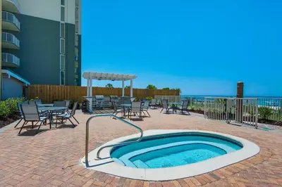 a hot tub on a patio with tables and chairs at Twin Palms 702 in Panama City Beach