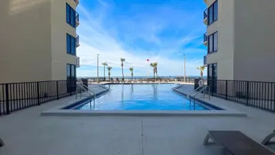 a swimming pool between two buildings with palm trees at Sunbird Resort 10th Floor Amazing Sunsets - by Sunbird Rentals in Panama City Beach