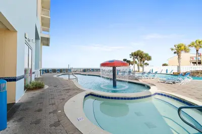 a swimming pool with an umbrella and chairs and a beach at Majestic Beach Towers Resort by Panhandle Getaways in Panama City Beach