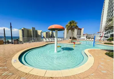 a fountain in the middle of a pool with an umbrella in the water at Spacious 1-Bedroom! Ocean Views & 5 Pools Resort! by Dolce Vita Getaways PCB in Panama City Beach