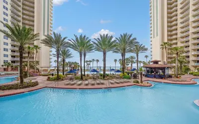 a large swimming pool with palm trees and buildings at Spacious 2-Bedroom Condo Beachfront Resort! By Dolce Vita Getaways PCB! in Panama City Beach