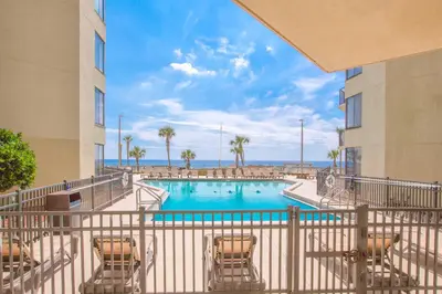 a swimming pool with chairs and the ocean in the background at Sunbird Beach Resort #902 West in Panama City Beach