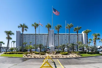 a building with palm trees and an american flag at Ocean View Retreat - Beachfront Bliss in Panama City Beach