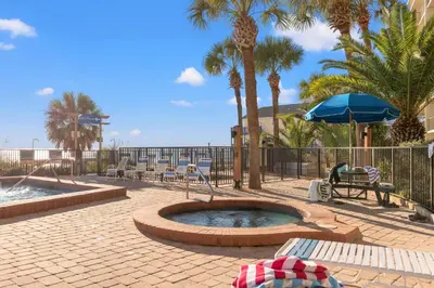 a patio with a pool and chairs and palm trees at Commodore 0608 in Panama City Beach