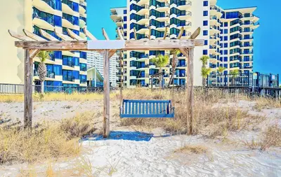 a bench on the beach in front of a building at Sunbird low Floor 2BR! Free Beach Chair Service! by Dolce Vita Getaways PCB in Panama City Beach