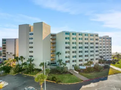 a large white building with palm trees in a parking lot at Beach Front Ocean View Condo - Top of the Gulf 105 in Panama City Beach