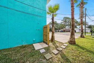 a blue building with a wooden door next to palm trees at Pool + Games + Outdoor Dining + Walk to the Beach in Panama City Beach