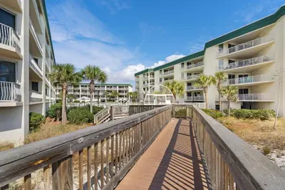 a boardwalk between two apartment buildings with palm trees at 4th-floor condo with beach ambience lagoon pool gym tennis & pickleball in Santa Rosa Beach