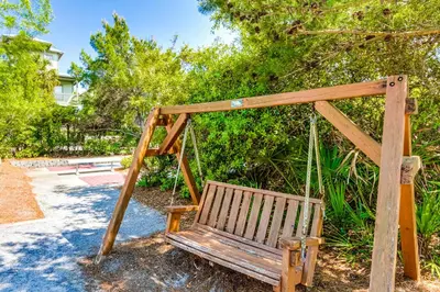 a wooden swing sitting in a yard with trees at Conveniently located Gulf condo with spacious layout pool & pickleball in Seacrest