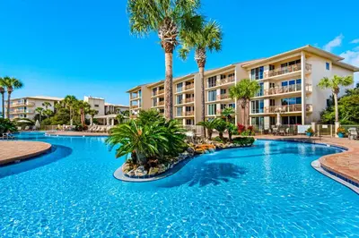 a swimming pool with palm trees in front of a building at Beach haven with patio lagoon pool hot tub & pickleball - walk to beach in Seacrest