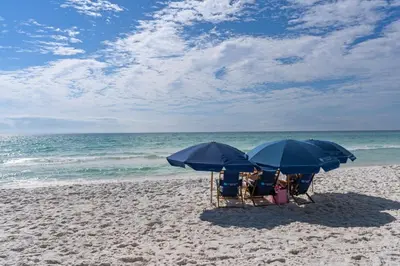 two chairs and blue umbrellas on a beach at Dunes of Seagrove condo with pool hot tub sauna gym & tennis pickleball in Santa Rosa Beach