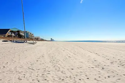 a beach with footprints in the sand and a house at Vista del Mar I Rest-A-While 201 in Panama City Beach