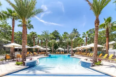 a pool with chairs and palm trees at the resort at Magnolia Cottages by the Sea by Panhandle Getaways in Watersound Beach