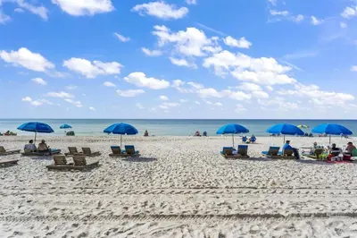 a group of people sitting on a beach with blue umbrellas at The Summit 616 in Panama City Beach