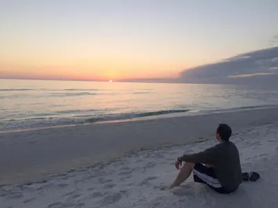 a man sitting on the beach watching the sunset at Edgewater 3-0413 'Once Upon A Tide' in Panama City Beach