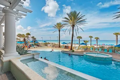 a pool at a resort with palm trees and the ocean at Boardwalk 1405 in Panama City Beach