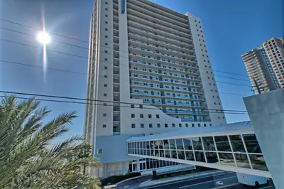 a tall white building with palm trees in front of it at Sterling Breeze - Cozy Beachfront One Bedroom Condo in Panama City Beach