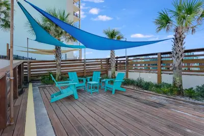 a deck with blue tables and chairs and palm trees at Top of The Gulf 213 in Panama City Beach