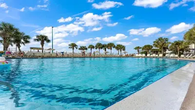a swimming pool with palm trees and a blue sky at The Summit 1031 in Panama City Beach