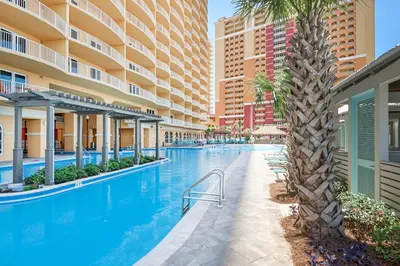 an infinity pool with a palm tree and buildings at Calypso 3-2307 in Panama City Beach