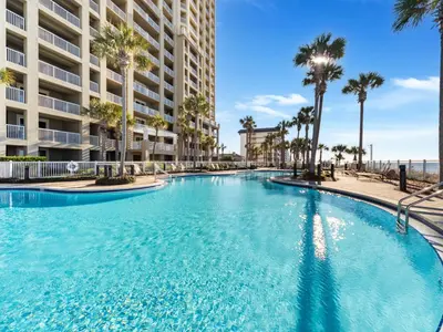a large swimming pool with palm trees in front of a building at Grand Panama Beach Resort - The Grand #1304 in Panama City Beach