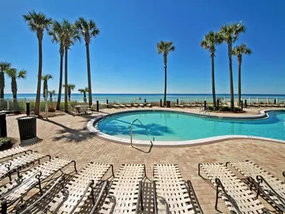 a pool with chairs and palm trees and the ocean at Grand Panama Beach Resort - The Grand #403 in Panama City Beach