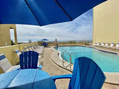 a pool with blue chairs and a table with an umbrella at Continental Condominiums 3 in Panama City Beach