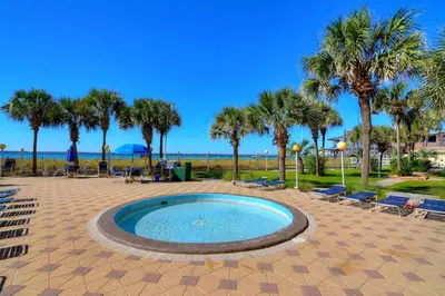 a pool with chairs and palm trees and the ocean at Summit Beach Resort 1230 in Panama City Beach