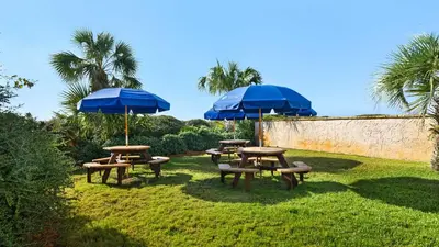 three picnic tables with blue umbrellas on the grass at Beachcrest 1002 in Santa Rosa Beach