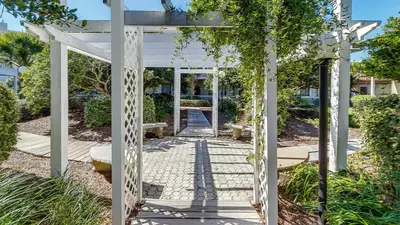 a white pergola in a garden with a walkway at Beachwood Villas 3H in Santa Rosa Beach