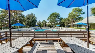 two picnic tables with umbrellas in front of a pool at Beachwood Villas 7F in Santa Rosa Beach