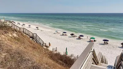 a beach with umbrellas and people sitting on the sand at Float Away in Panama City Beach