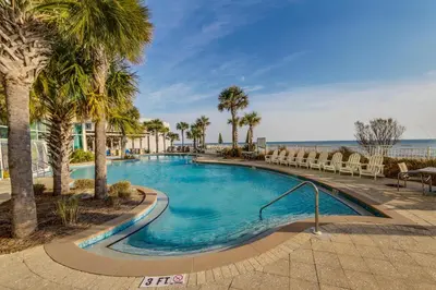 a swimming pool with palm trees and chairs at Aqua Resort 811 in Panama City Beach
