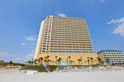 a large yellow building on the beach with palm trees at Sterling Reef 1704 in Panama City Beach